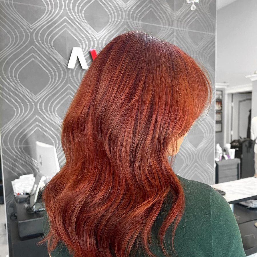 Woman's long copper-red hair with layers, at the Avalon Salon front desk in Calgary